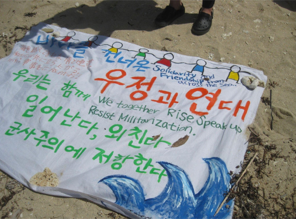 Figure 11. WE TOGETHER RISE
Banner made by Korean women for a public protest against US base expansion at Henoko, Okinawa, 2017. Fabric markers on cotton cloth. Photo: Gwyn Kirk