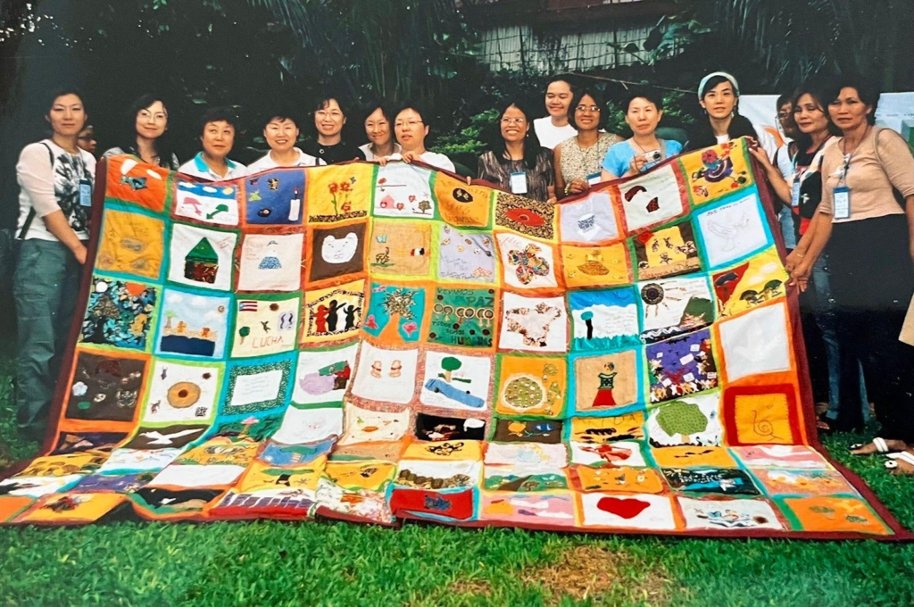 Figure 5. GENUINE SECURITY QUILT In the fall of 2002, Network country groups each did coordinated actions around the same date. Some joined local anti-war rallies, others organized events, or wrote statements. The Puerto Rico group made this huge quilt in opposition to the US Navy bombing of Vieques and as a celebration of life. It took a whole suitcase to bring it to the next Network meeting in the Philippines in 2004, shown here with other Network members. Photo: Michiko Hase.